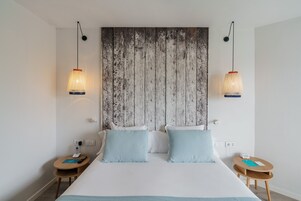 Una habitación de hotel con una cama grande, dos mesitas de noche, un cabecero de madera y lámparas colgantes.