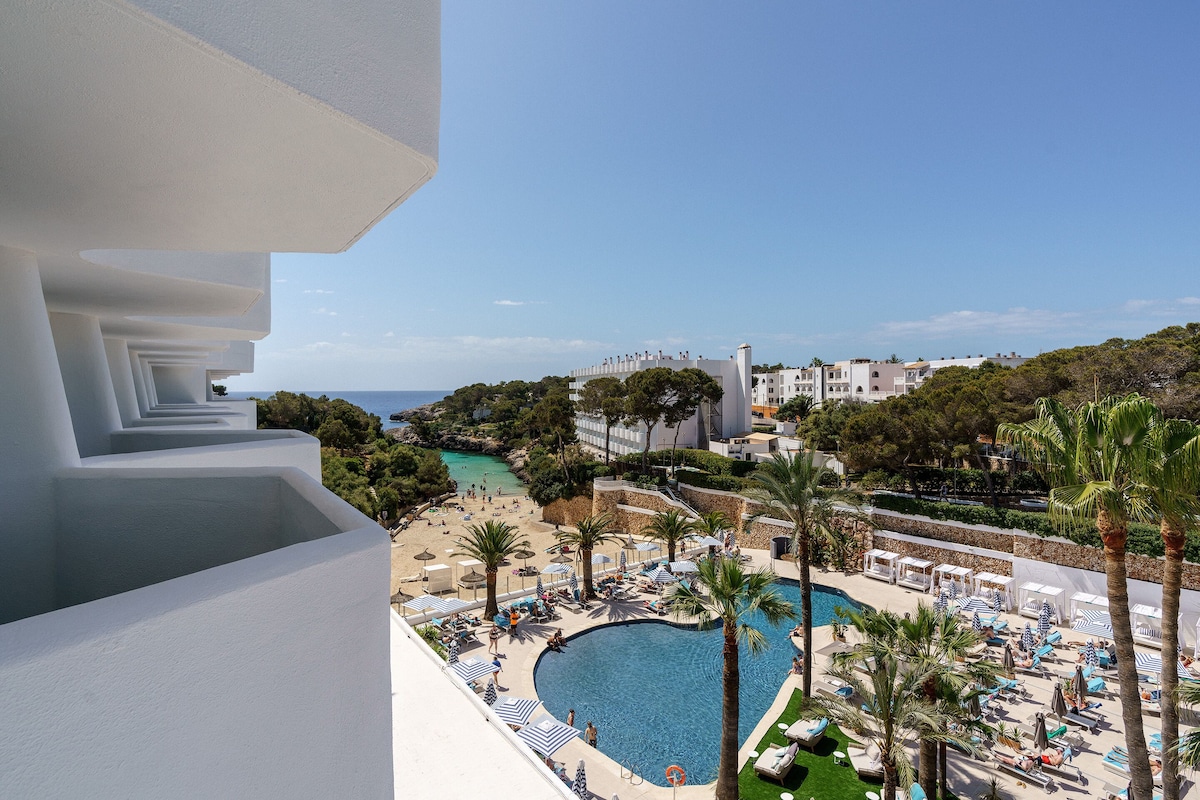 A resort with a pool area, palm trees, and a view of the sea.