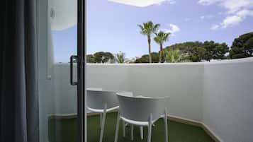 Puerta de cristal que da a un balcón con dos sillas blancas y césped artificial.