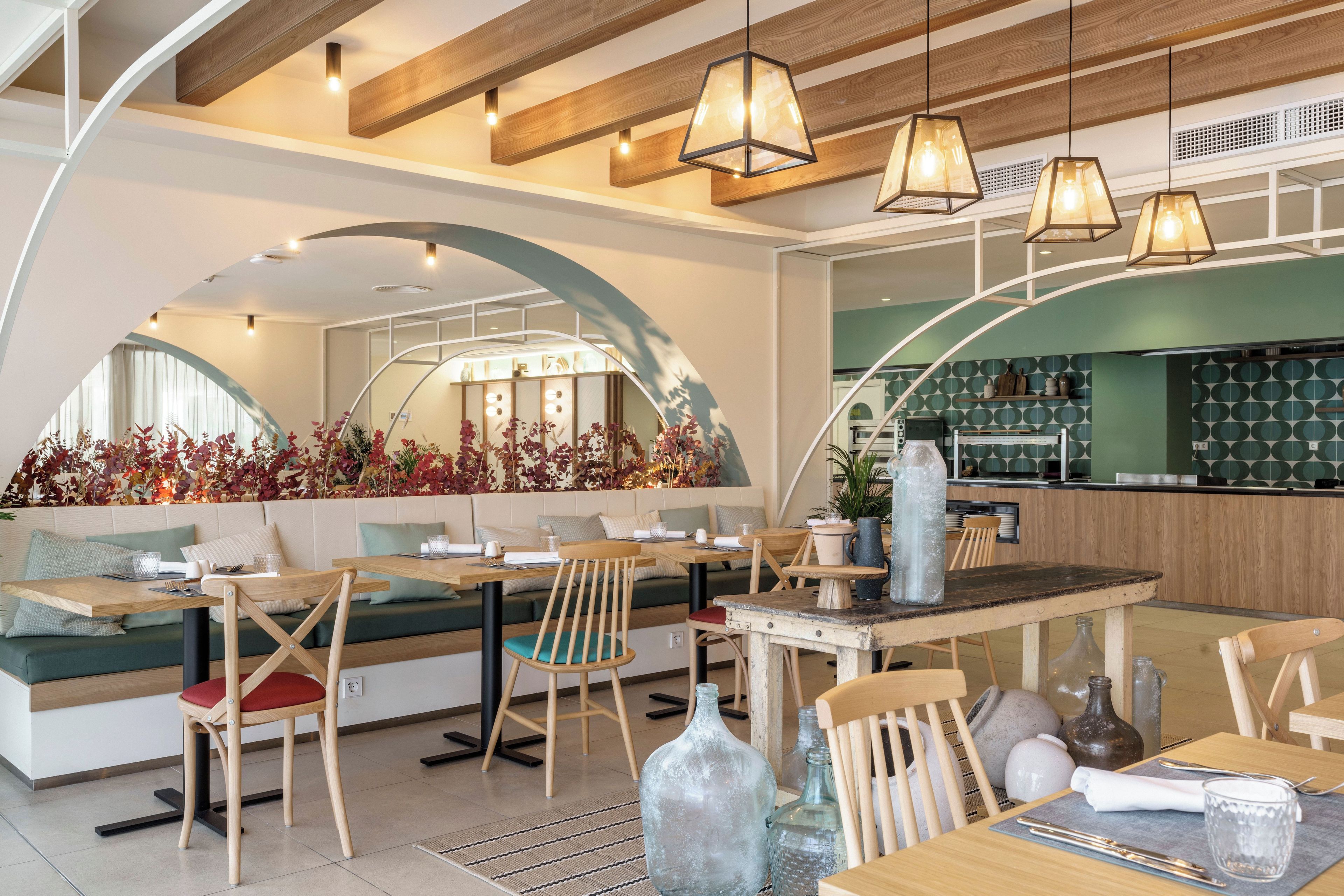 Interior moderno de restaurante con mobiliario de madera, iluminación colgante y salpicadero con azulejos verdes.