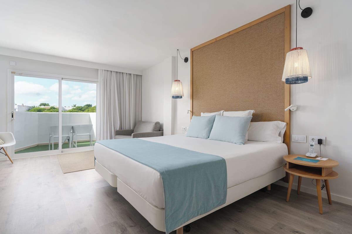 Una habitación de hotel moderna con una cama grande, una mesita con un teléfono y vistas al exterior.