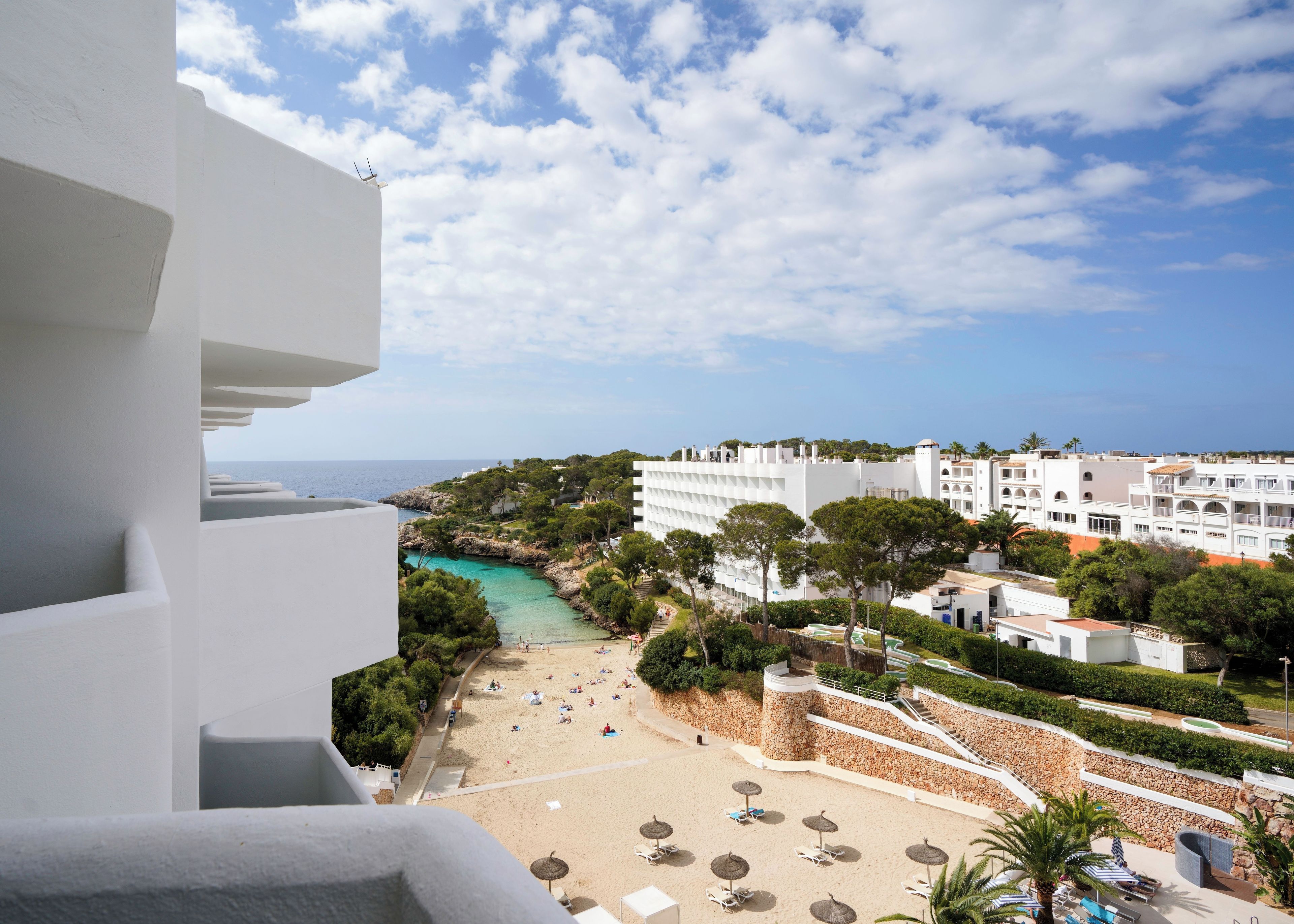 A coastal hotel with a beach view, multiple balconies, and a pool area.