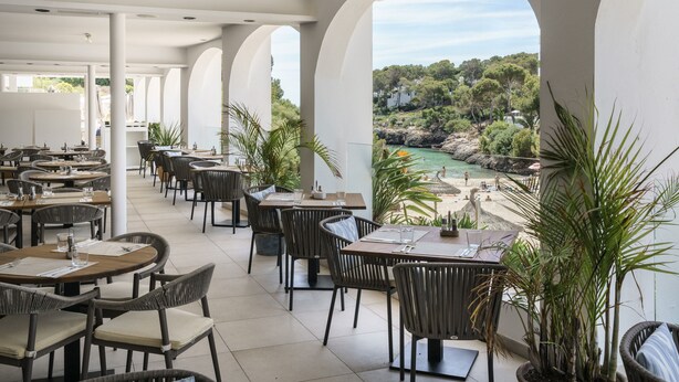 Un restaurant doté d’une terrasse, de colonnes blanches et offrant une vue sur la plage et la végétation.
