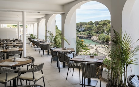A restaurant with outdoor seating, white pillars, and a view of the beach and greenery.
