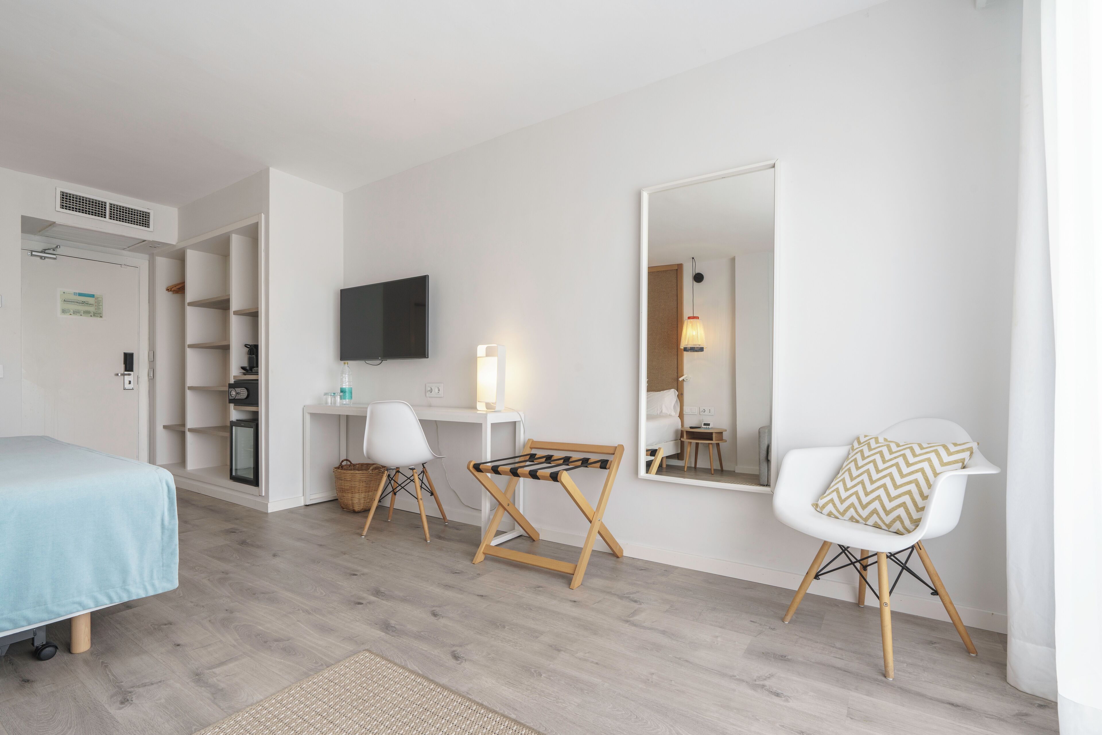 Una habitación de hotel moderna con una cama, un escritorio con ordenador, una silla, un televisor y un espejo grande.