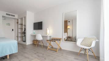 Una habitación de hotel moderna con una cama, un escritorio con ordenador, una silla, un televisor y un espejo grande.