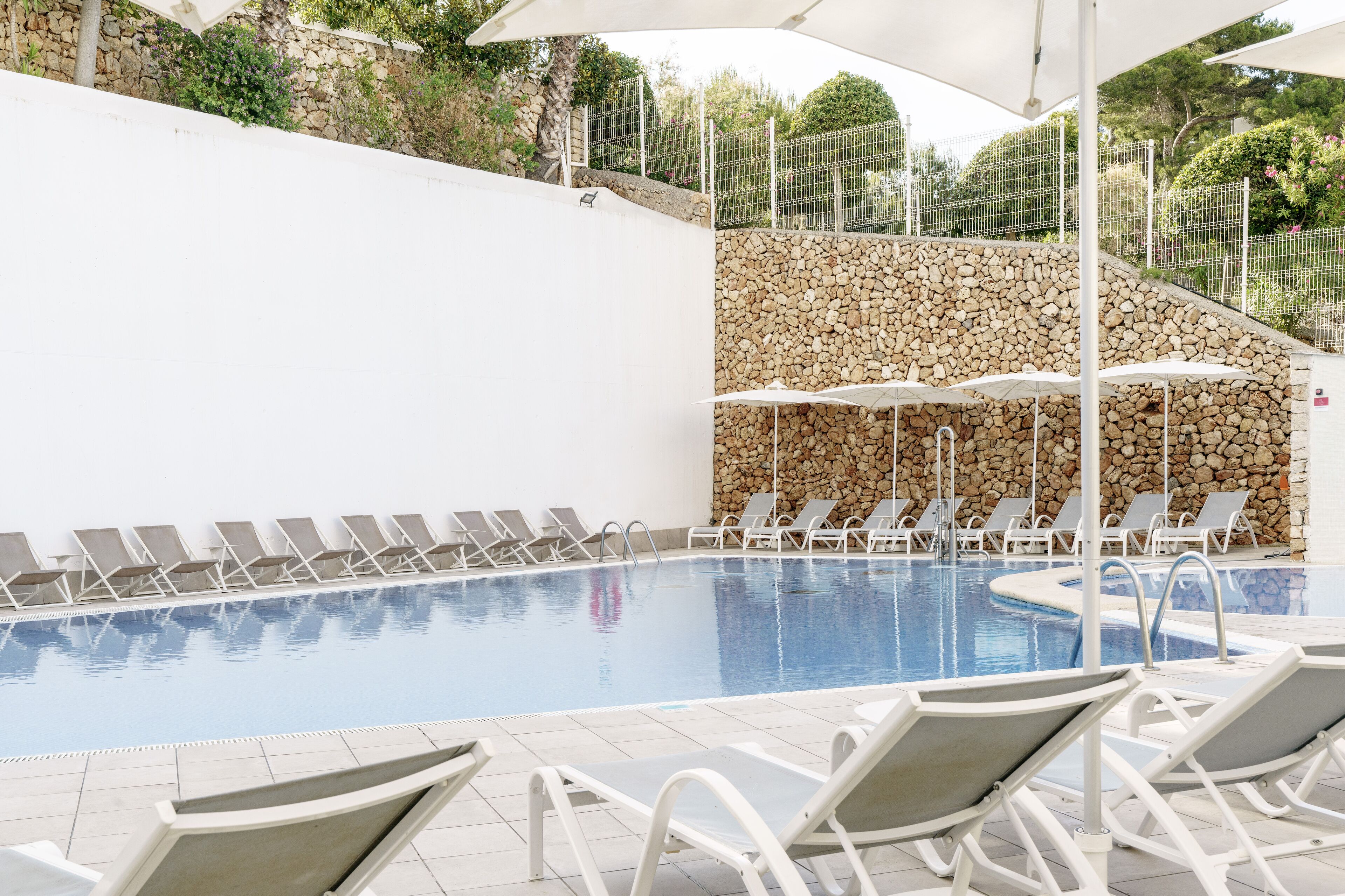 A swimming pool with white tiled floor and surrounding white lounge chairs.