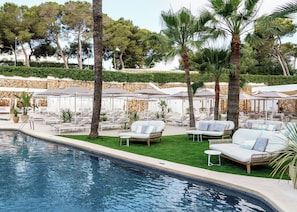A poolside area with lounge chairs, umbrellas, and a stone wall. - AluaSoul Mallorca Resort - Adults Only - Hyatt Inclusive Collection (Santanyi)