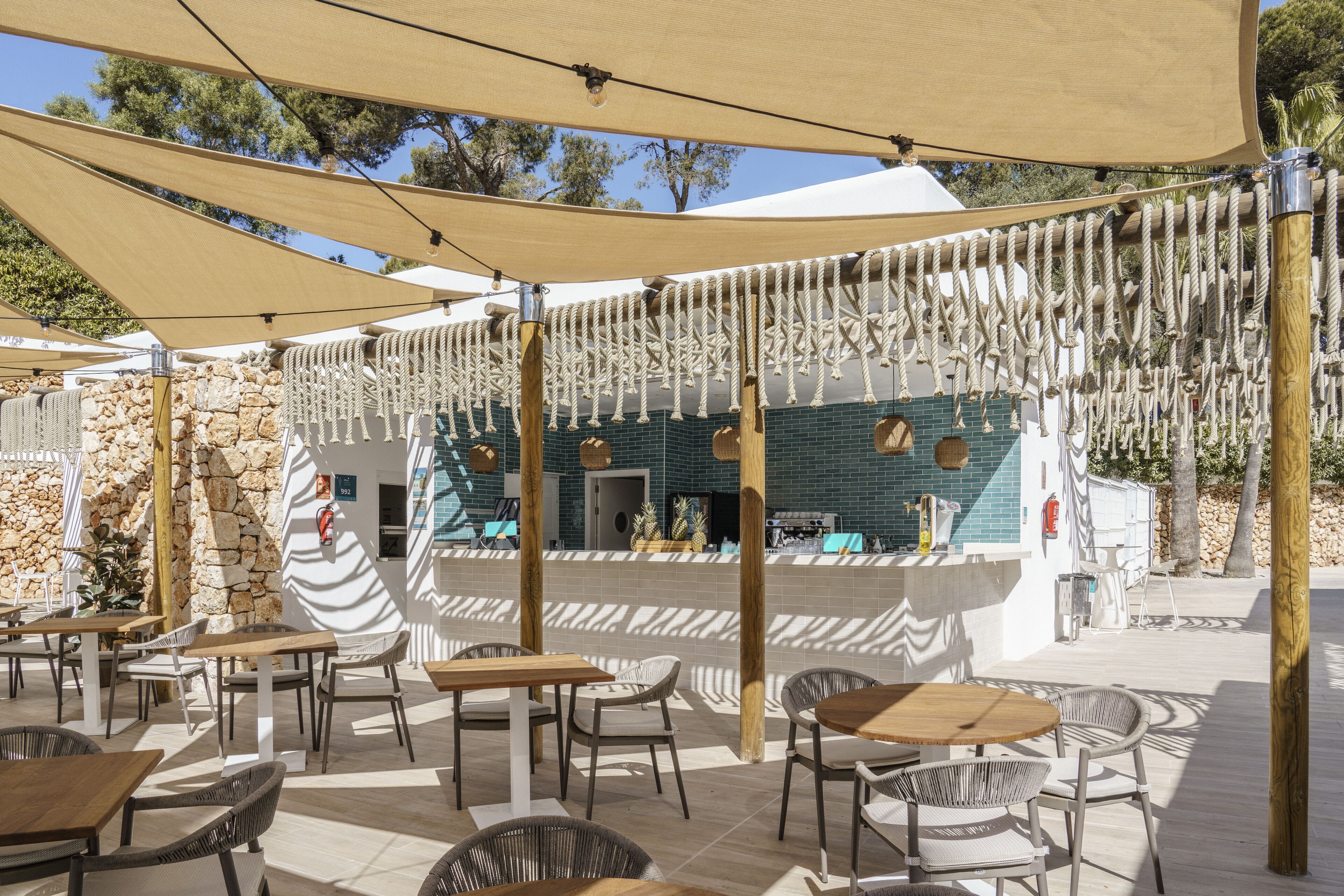 An outdoor café with tables and chairs, a stone wall, and a bar area with a blue tiled wall.