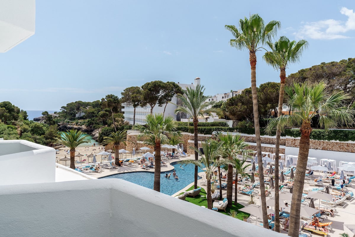 Zona de piscina con sillones de descanso y sombrillas, rodeada de palmeras y vistas al mar.