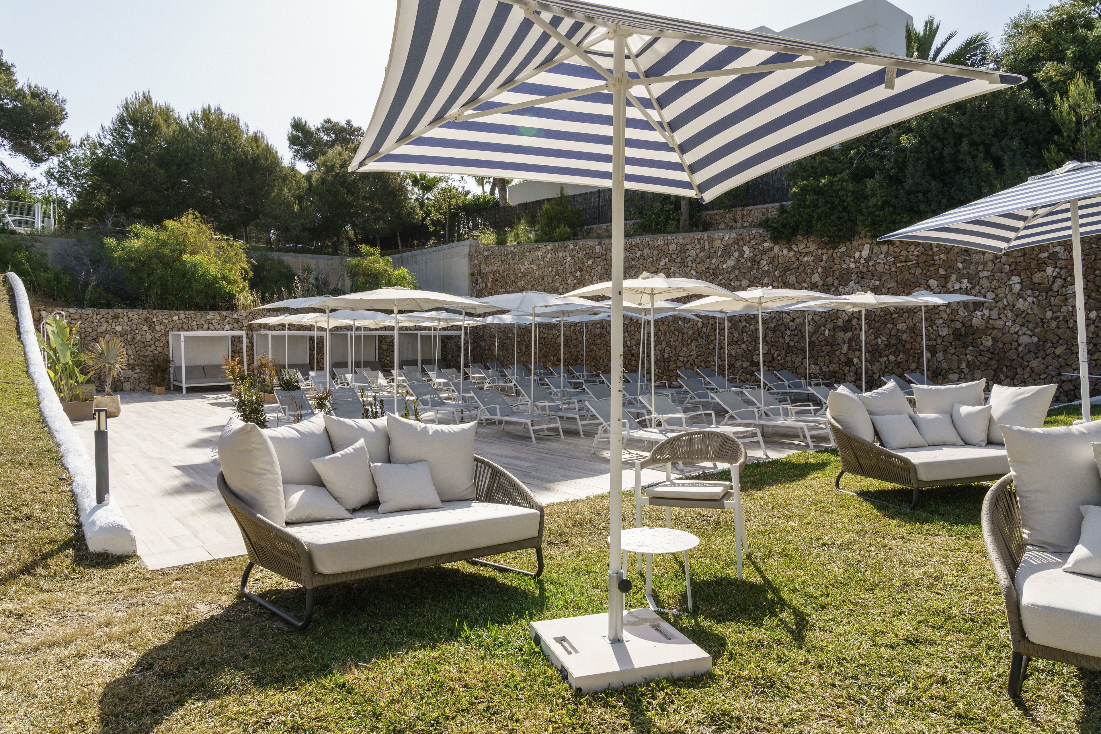 Eine Terrassenfläche mit Sitzgelegenheiten im Freien, darunter Sofas und Stühle, unter gestreiften Sonnenschirmen.