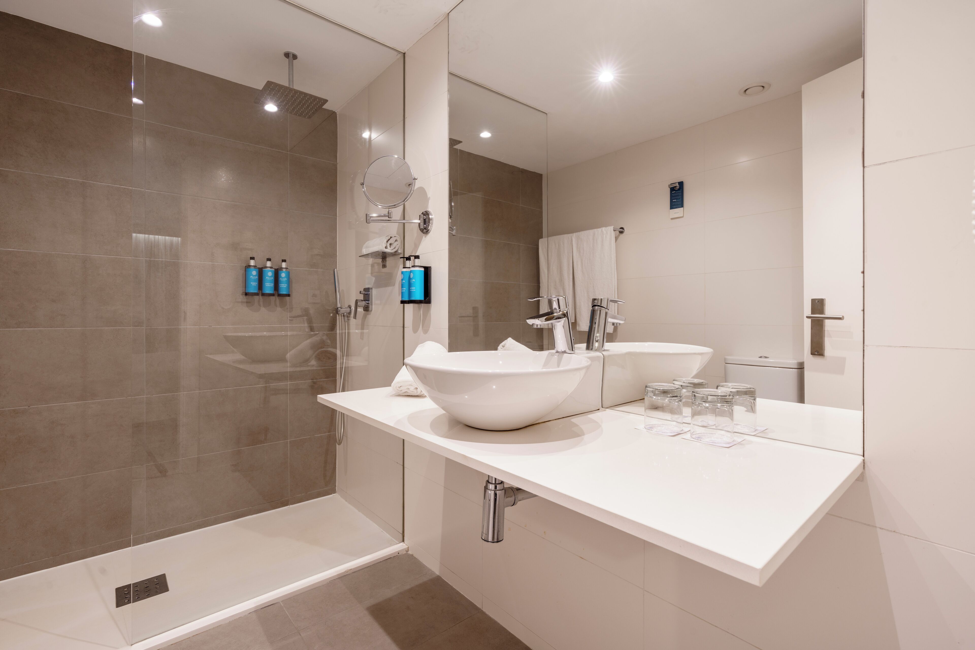 Ein modernes Badezimmer mit einem großen, weißen Waschbecken, einer Duschkabine aus Glas und einem Spiegel über dem Waschbecken.