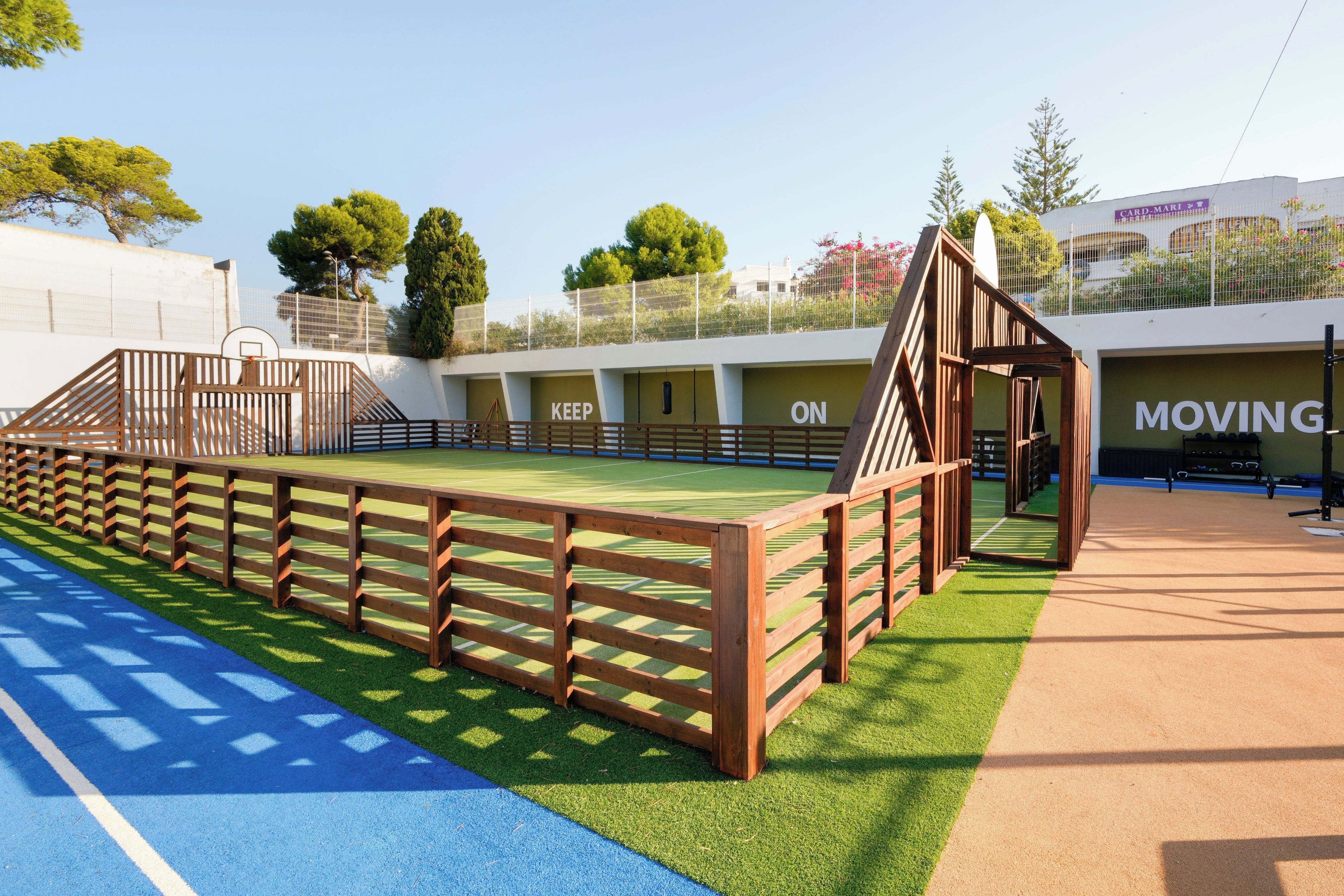 A sports facility with a multi-sport court, wooden fencing, and a building labeled 'KEEP ON' and 'MOVING'.