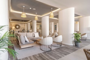 A spacious living area with a sofa, chairs, and a coffee table. There are large columns and pendant lights. - AluaSoul Mallorca Resort - Adults Only - Hyatt Inclusive Collection (Santanyi)