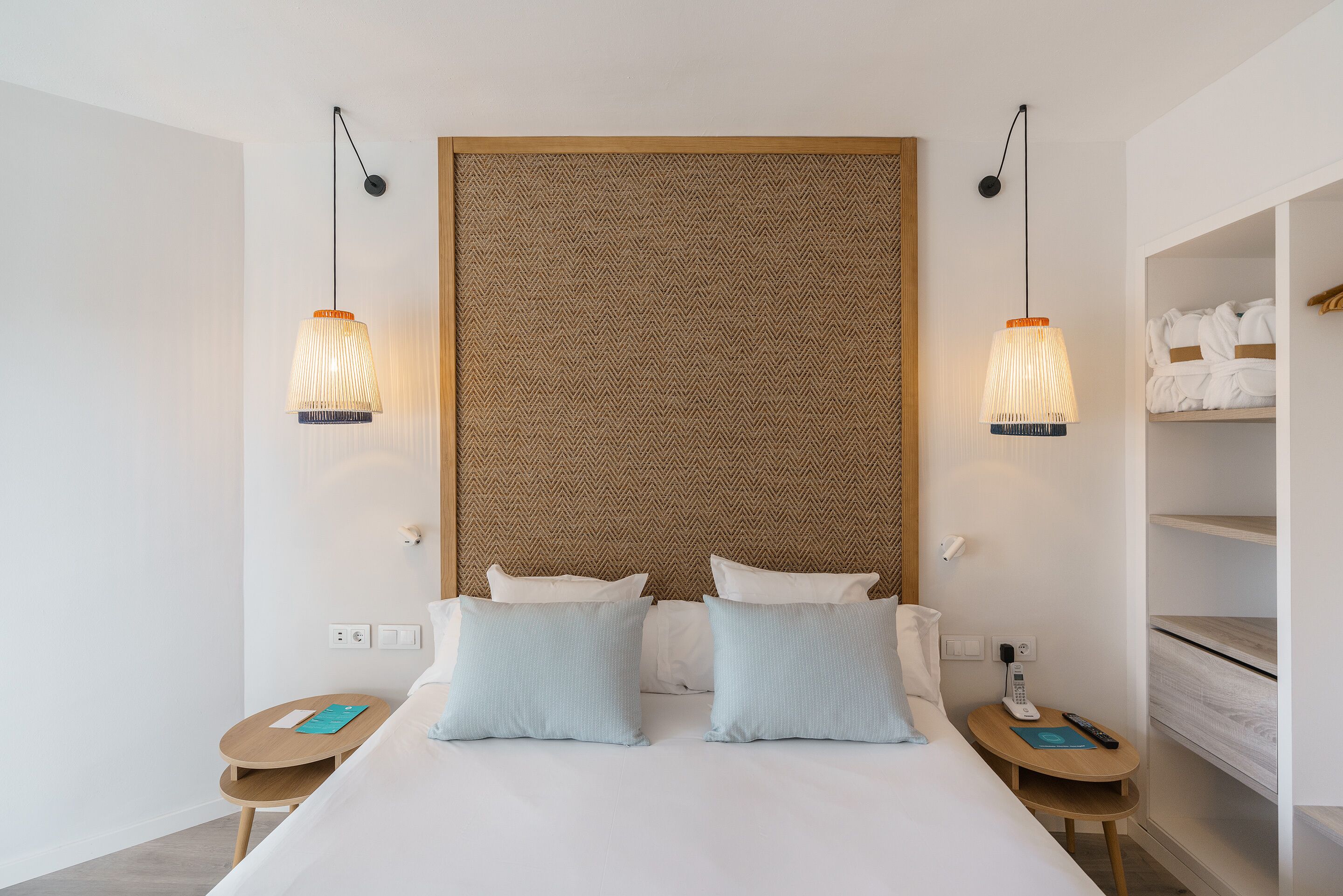 Una habitación de hotel moderna con una cama grande, dos mesitas de noche, un cabecero de madera y dos lámparas colgantes.