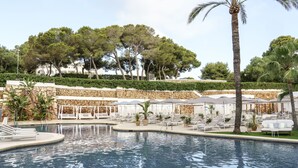 Une piscine entourée de murs de pierre et d’arbres, avec des chaises longues et des parasols.