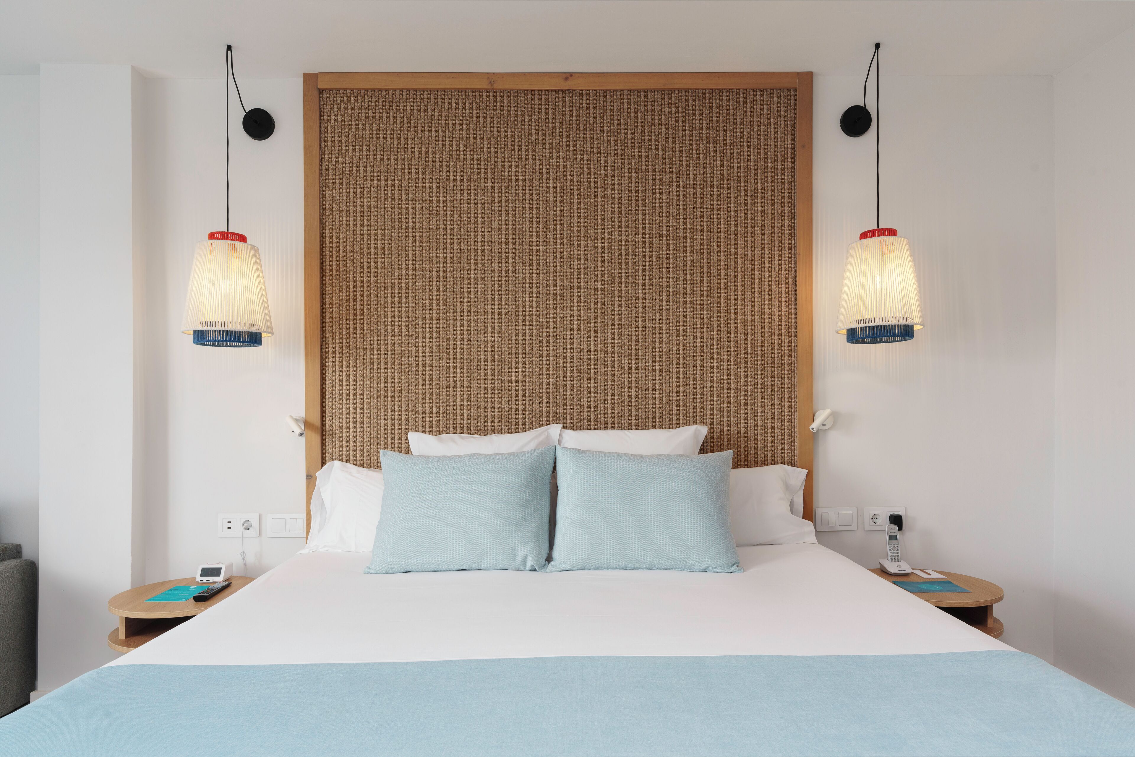 A hotel room with a large bed, two bedside tables, a telephone, and two pendant lights.
