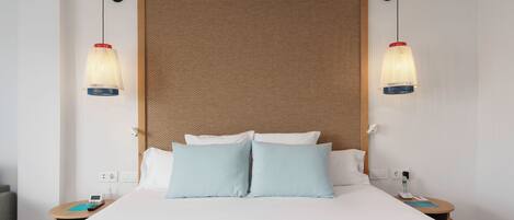 A hotel room with a large bed, two bedside tables, a telephone, and two pendant lights.
