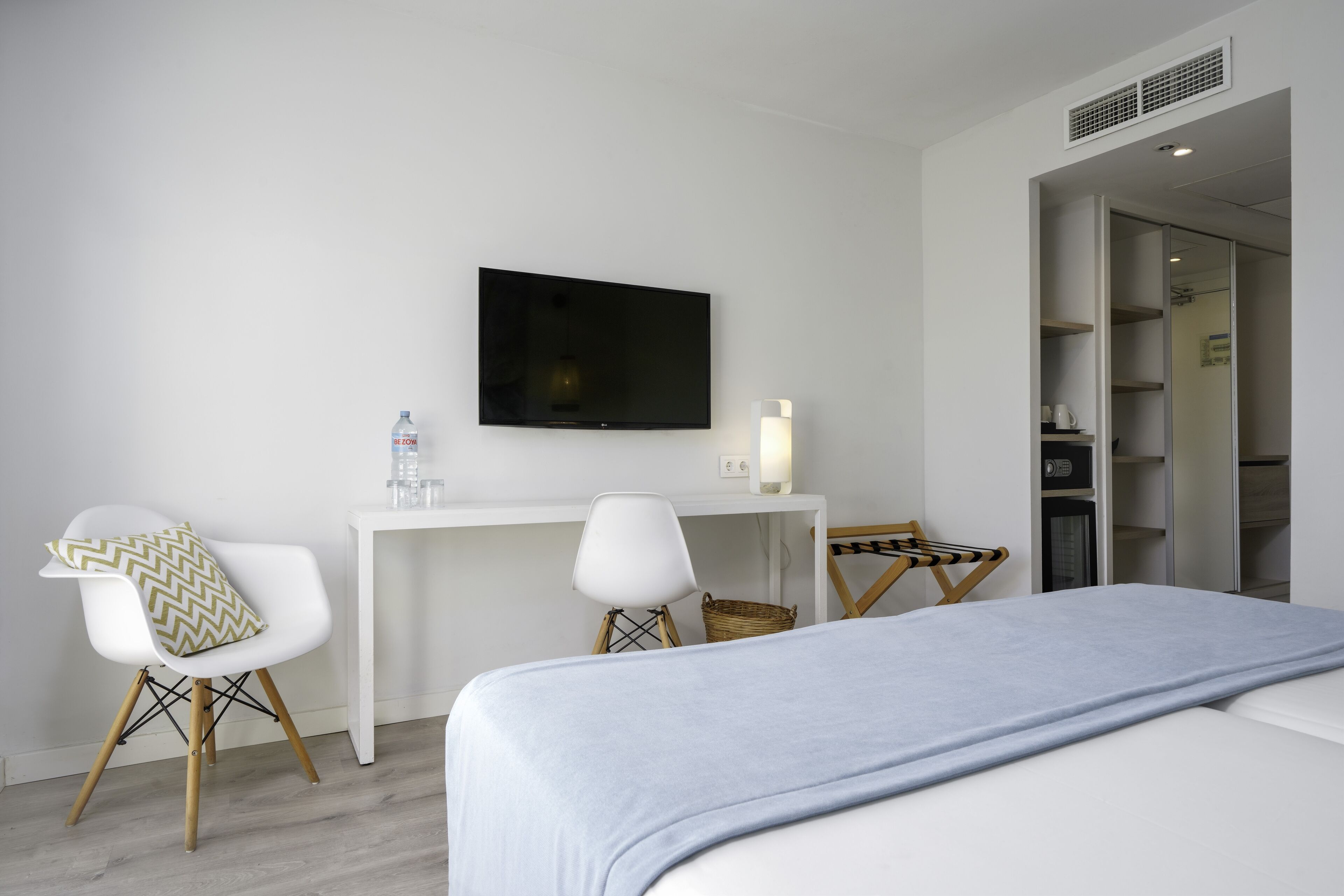 A modern hotel room with a bed, a desk, two chairs, a television, and a wardrobe.