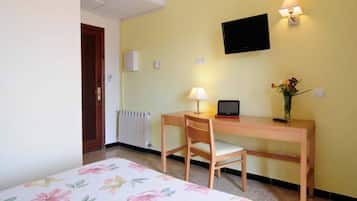A room with a bed, a desk with a chair, a TV mounted on the wall, and a lamp.