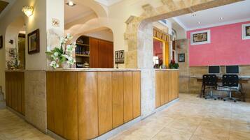 A reception area with a wooden reception desk, a marble-tiled floor, and a pink wall with framed artwork.