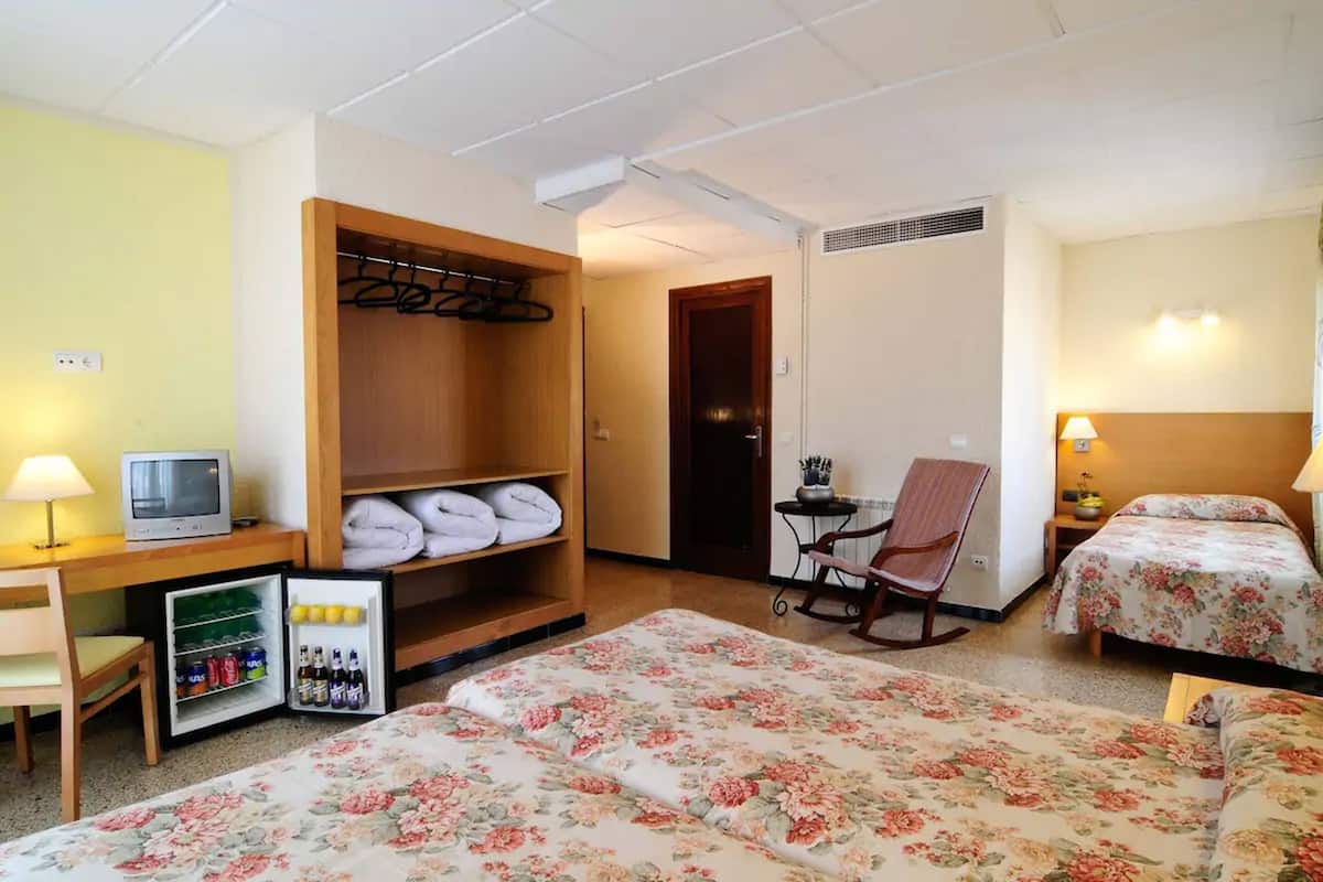A hotel room with two beds, a desk with a television, a mini-fridge with beverages, and a chair.
