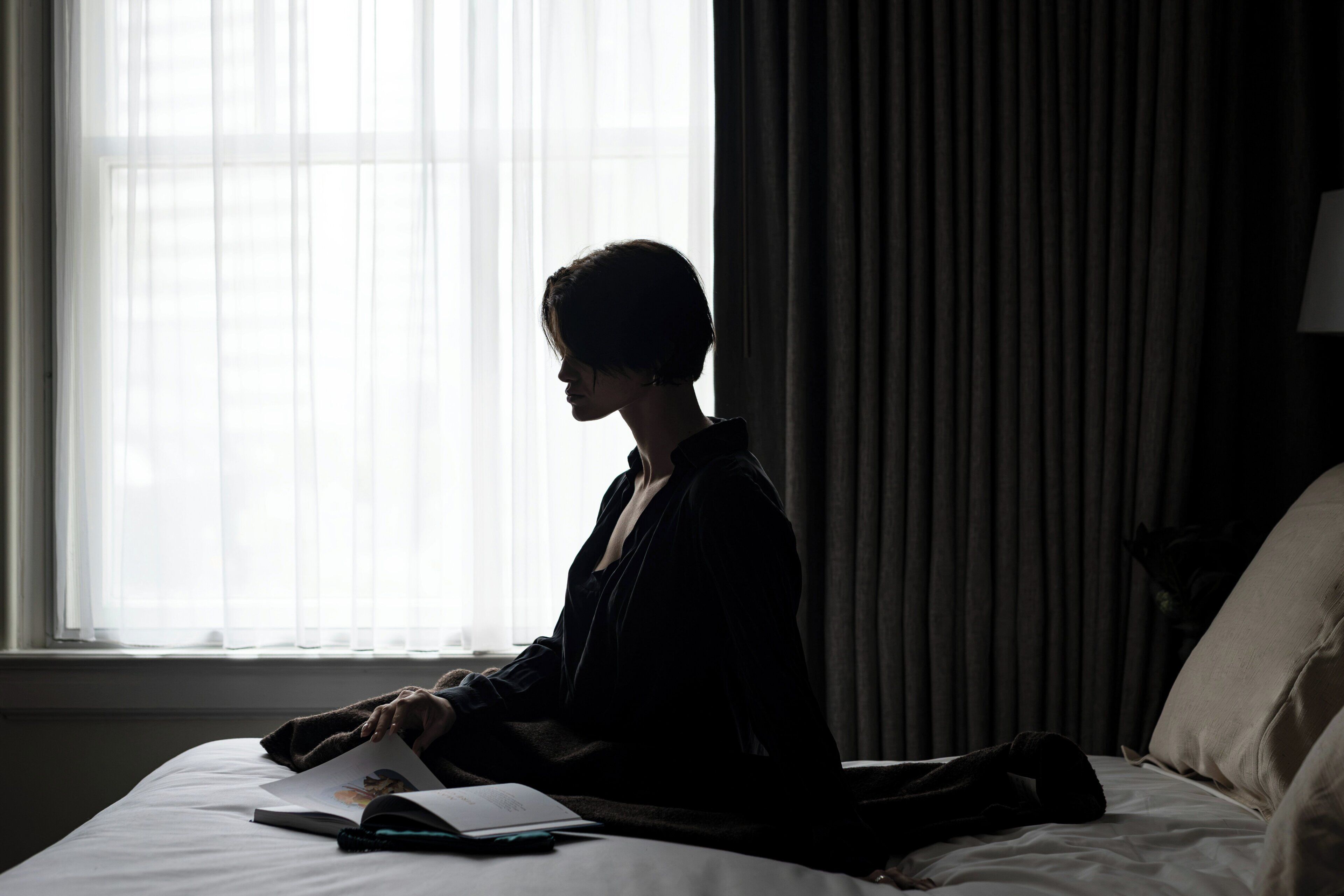 A person sitting on a bed in a room with a window and curtains.