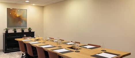 A conference room with a long table, chairs, and a cabinet with potted plants.
