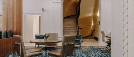 A hotel lobby with a round table, two chairs, a staircase, and a patterned carpet.