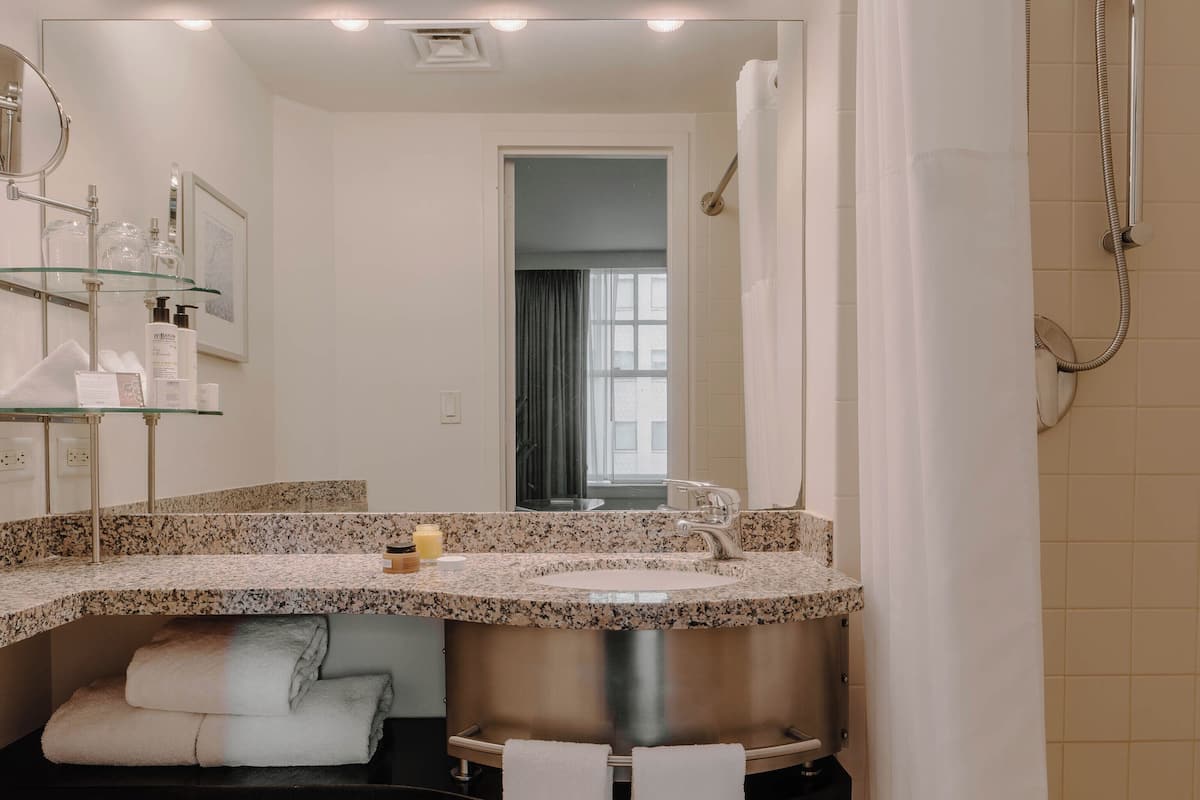 A modern bathroom with a granite countertop sink, a large mirror, and a shower with a curtain.