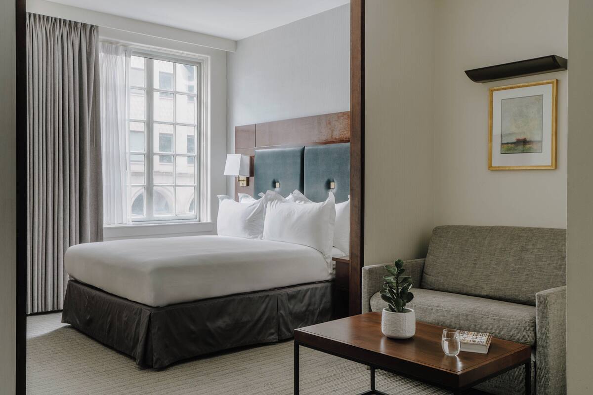 A hotel room with a large bed, a sofa, a coffee table, and a window with curtains.