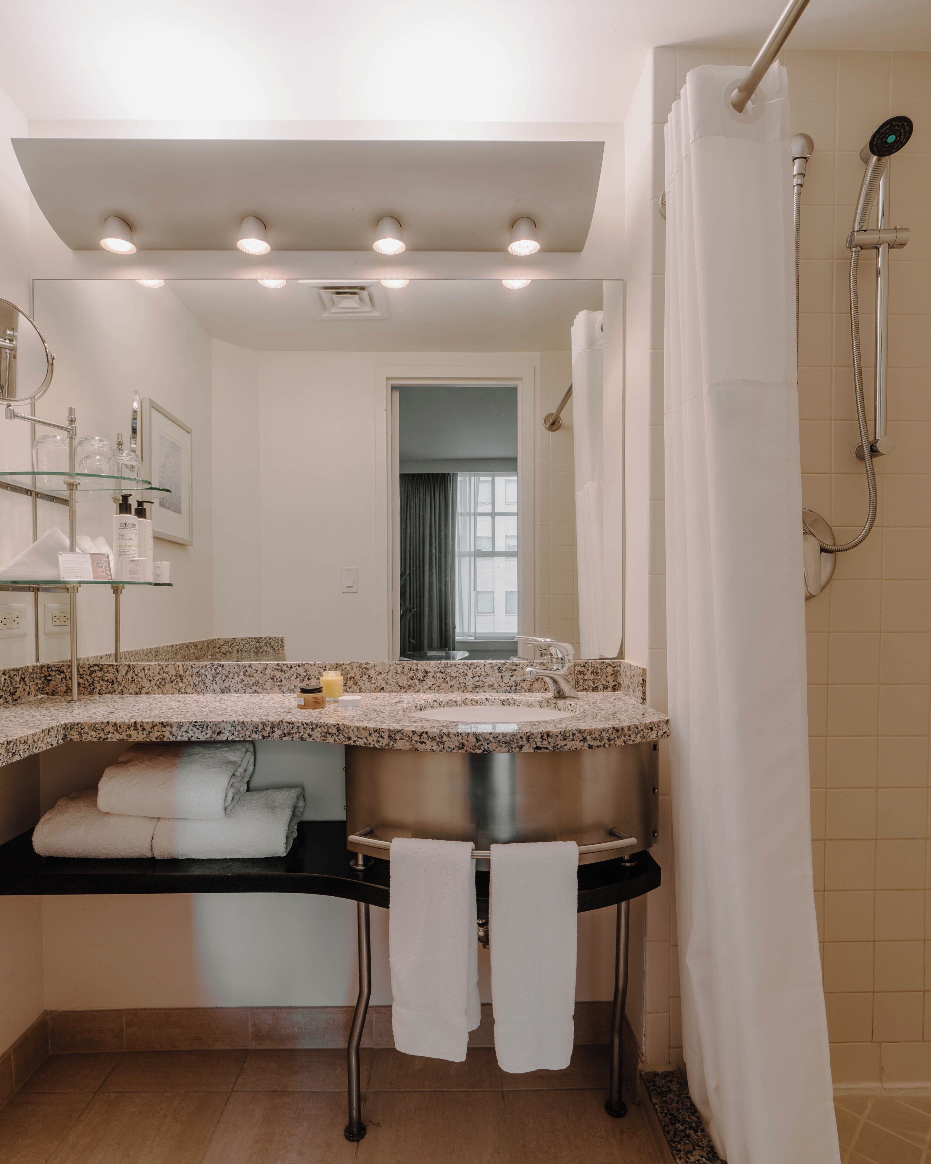 Un baño con lavamanos de encimera de granito, un espejo, ducha con cortina y una ventana.