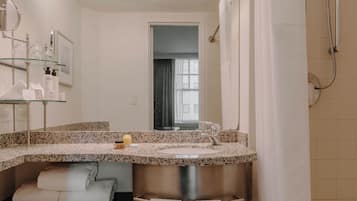 Un baño con lavamanos de encimera de granito, un espejo, ducha con cortina y una ventana.