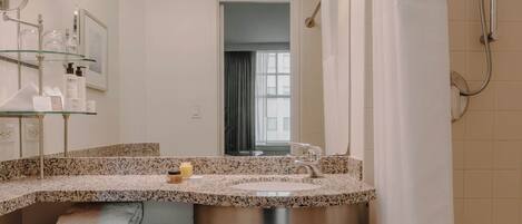 A bathroom with a granite countertop sink, a mirror, a shower with a curtain, and a window.