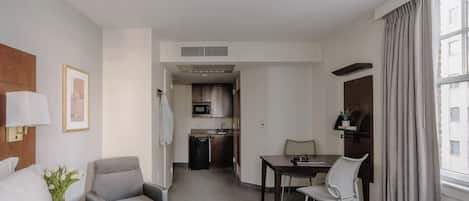 Une chambre d’hôtel équipée d’un lit, d’un bureau, d’une chaise, d’une petite kitchenette et d’une fenêtre avec des rideaux.