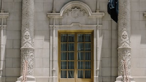 A building facade with three windows, each with a wooden frame and green curtains. Decorative columns with intricate carvings flank the windows. - Club Quarters Hotel Downtown, Houston (Houston)