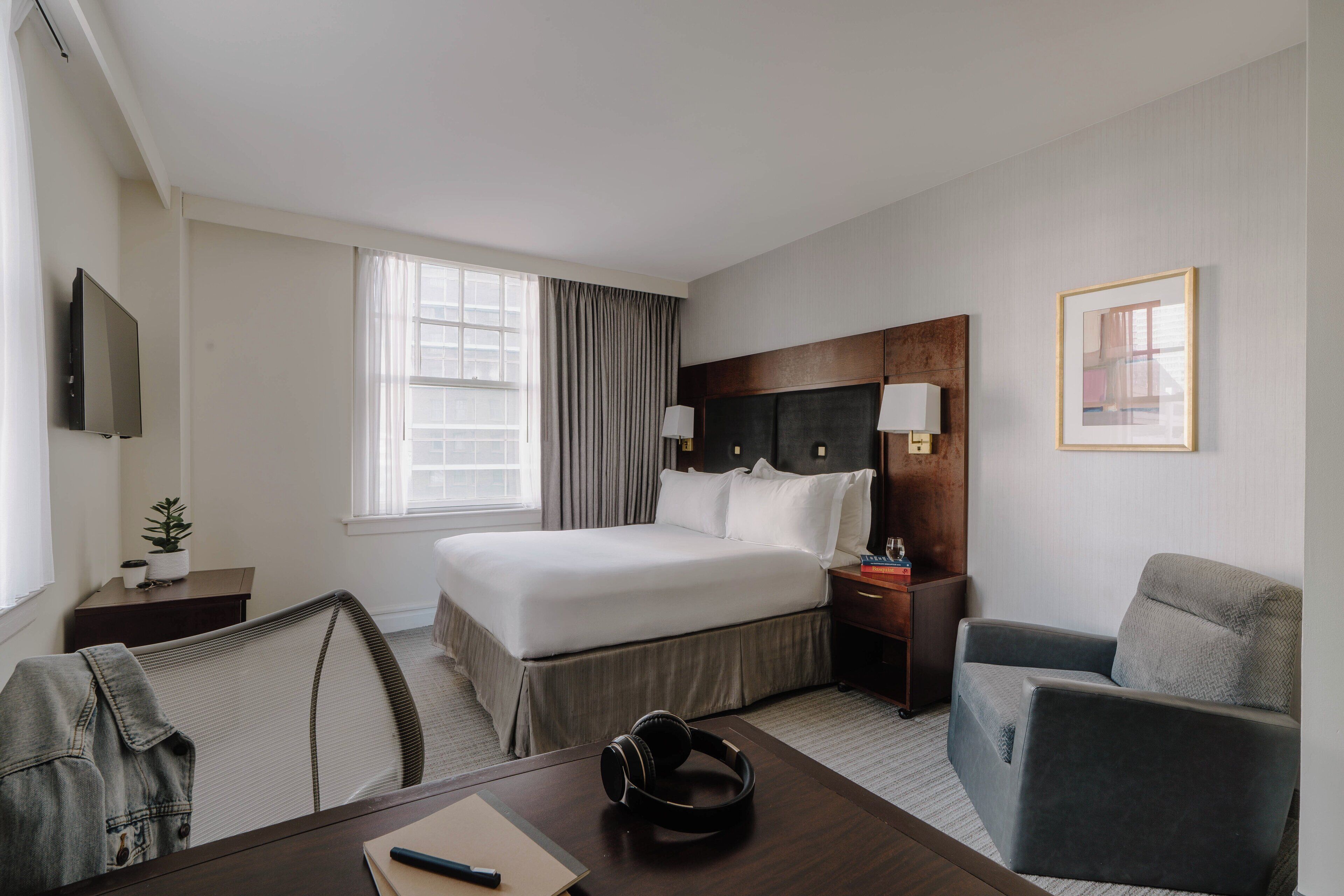 A hotel room with a large bed, a desk with a chair, a television, and a window with curtains.