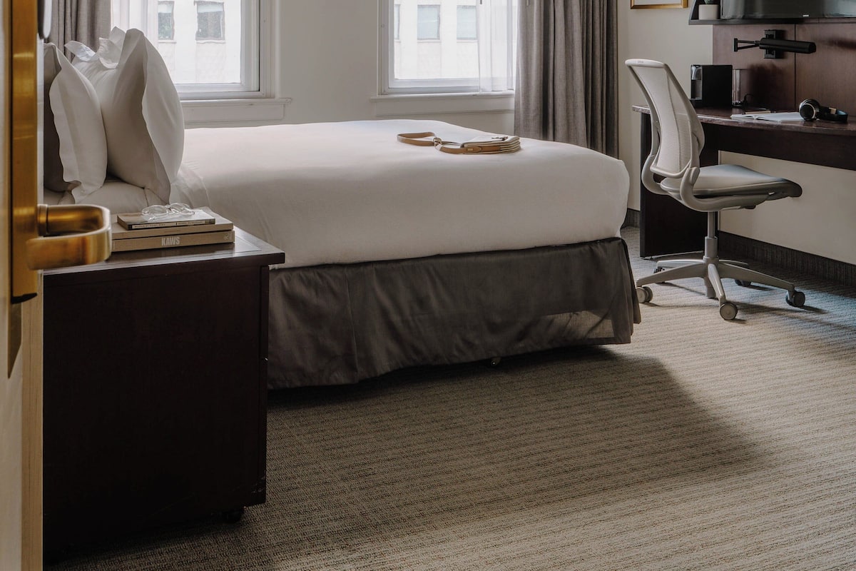 A hotel room with a large bed, a desk, a chair, a TV, and a window with curtains.