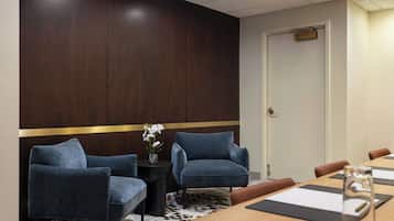 Una sala de conferencias con una pared de acento de madera, dos sillas azules, una pequeña mesa con un jarrón de flores blancas y una puerta con manija de latón.