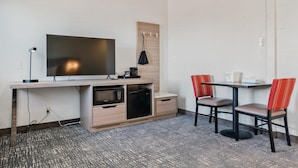 Ein modernes Zimmer mit Holzboden, einem Flachbildfernseher, einer Mikrowelle, einem Kühlschrank, einem kleinen Tisch mit zwei Stühlen und einem Holzschrank.