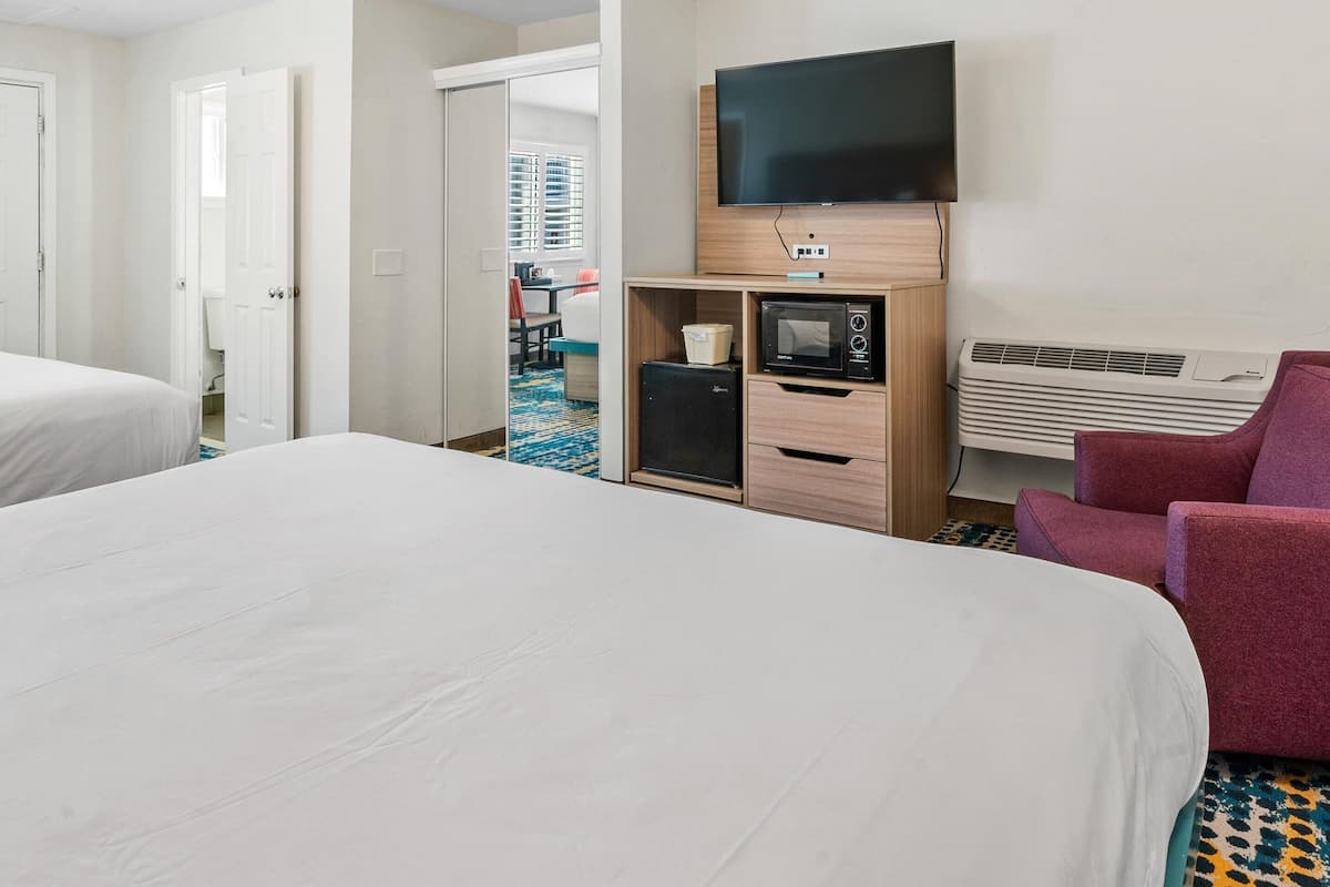 A hotel room with a bed, a TV mounted on the wall, a microwave, and a heater.