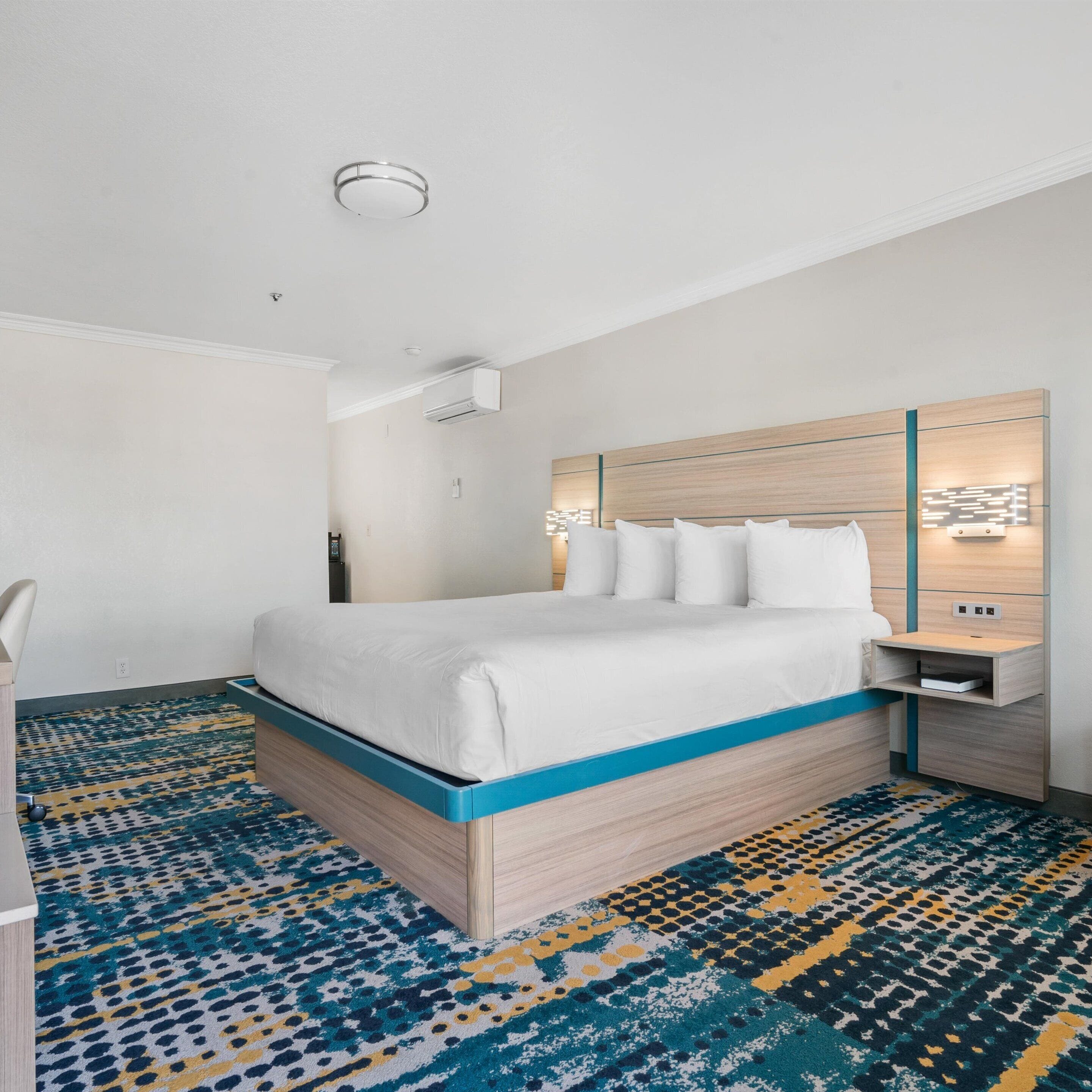 Una habitación de hotel moderna con una cama, una mesita de noche, una lámpara de pared y una alfombra estampada.
