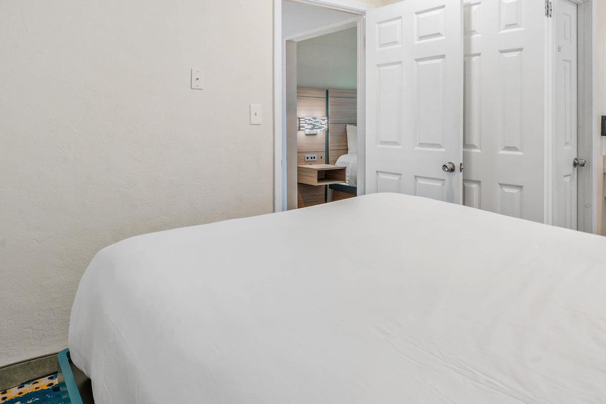 A bedroom with a large bed, a door leading to a bathroom, and a small desk.