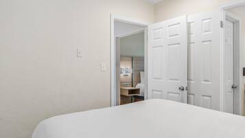 A bedroom with a large bed, a door leading to a bathroom, and a small desk.