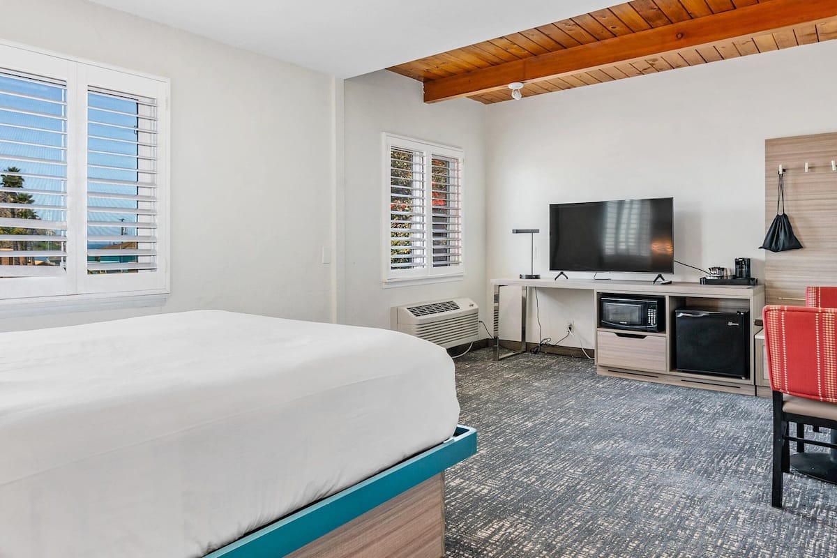 A hotel room with a bed, a TV, a desk, and a small fridge.