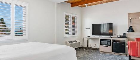Una habitación de hotel con una cama, televisión, escritorio y un refrigerador pequeño.