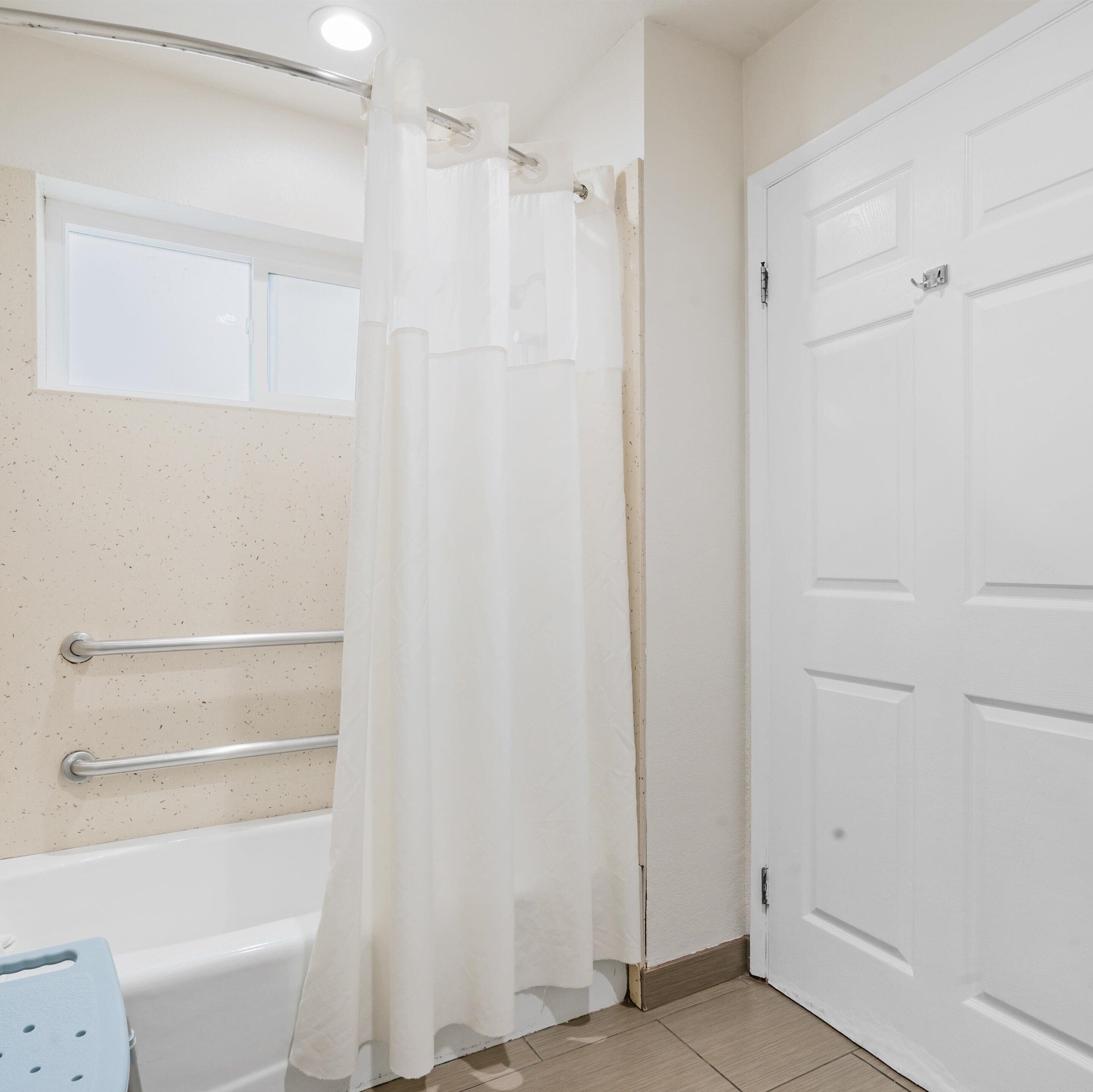 A bathroom with a bathtub, a shower curtain, a door, and a window.