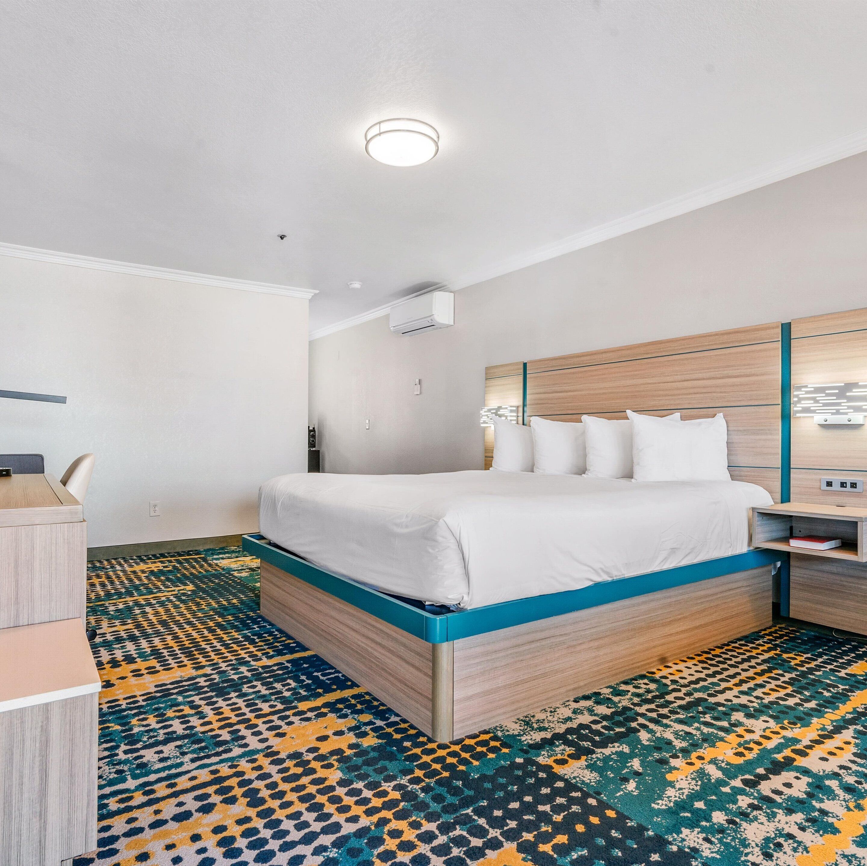 A hotel room with a bed, bedside table, and a desk with a chair.