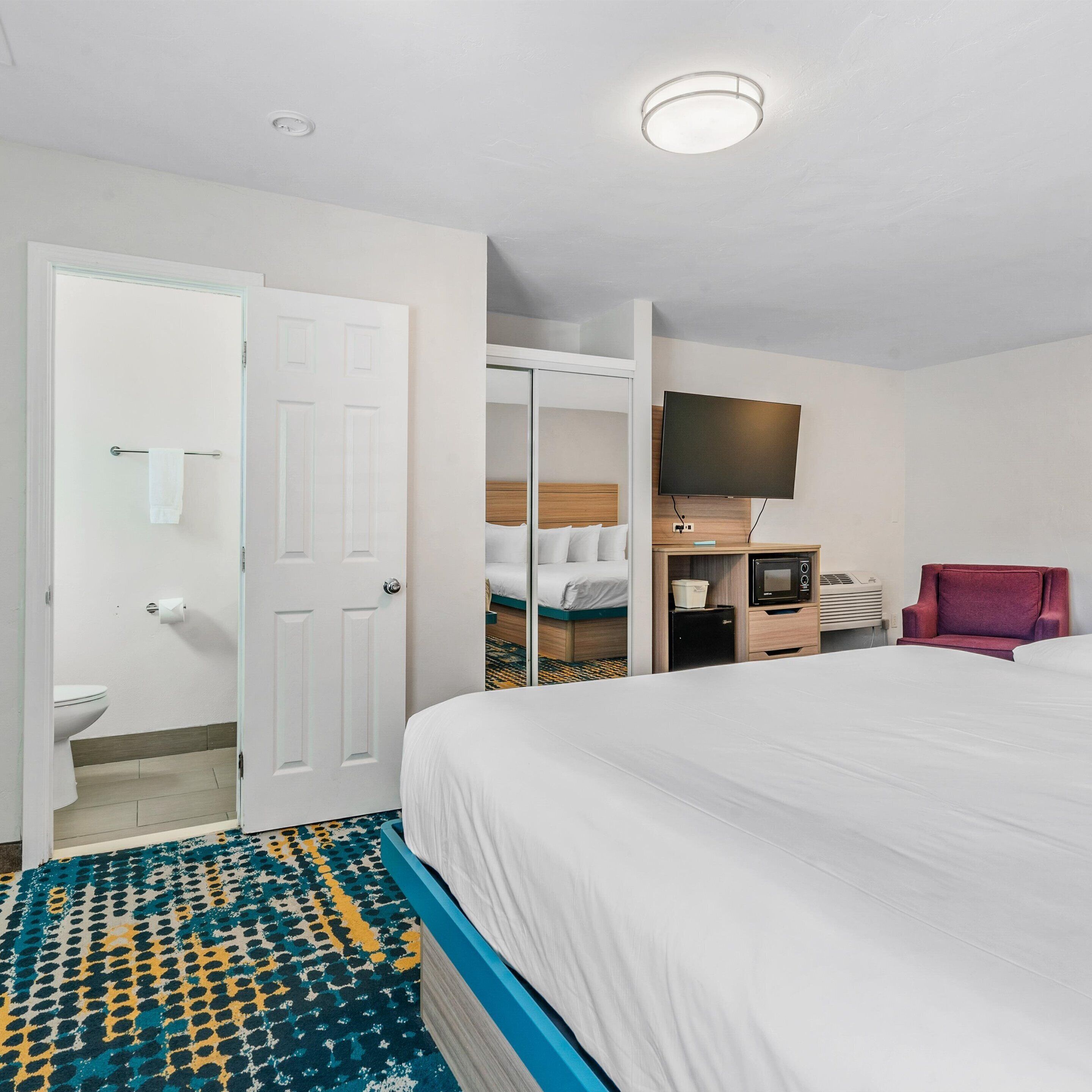 Habitación de hotel con cama, televisor, microondas y una silla roja.