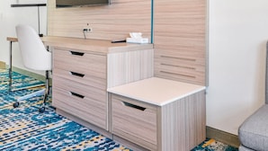 Ein modernes Hotelzimmer mit Schreibtisch aus Holz, einem großen Spiegel und einem Flachbildfernseher.